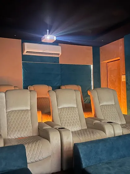 A 5.1.4 home cinema with a vibrant color scheme, featuring cream-colored recliners and a bold teal accent wall.