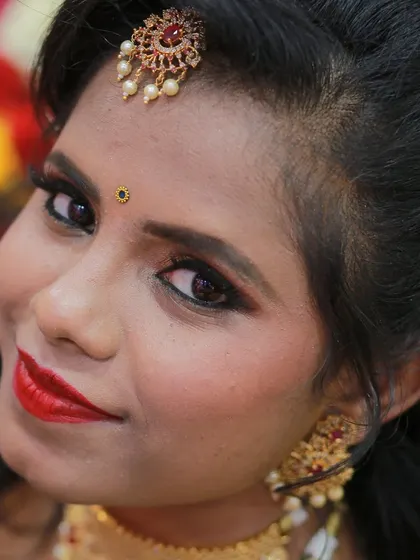 A lovely high-angle portrait инфекции a bride with bold red lipstick and traditional gold jewelry.
