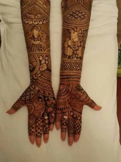 A full-arm bridal design featuring portraits of the bride on the forearms, surrounded by peacocks and intricate traditional patterns.