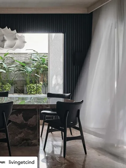 The dining room, where sheer curtains billow in the breeze, softening the dramatic, dark features of the space. The view into the green courtyard adds a sense of tranquility.
