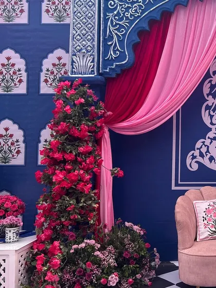 A cozy seating nook with a blush pink sofa, set against a royal blue wall with traditional floral motifs and draped pink curtains.