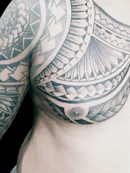A powerful Polynesian and tribal style tattoo covering the chest and shoulder. This type of work involves creating intricate, flowing patterns that complement the body's natural lines. Each symbol can hold personal meaning, telling a story on the skin.