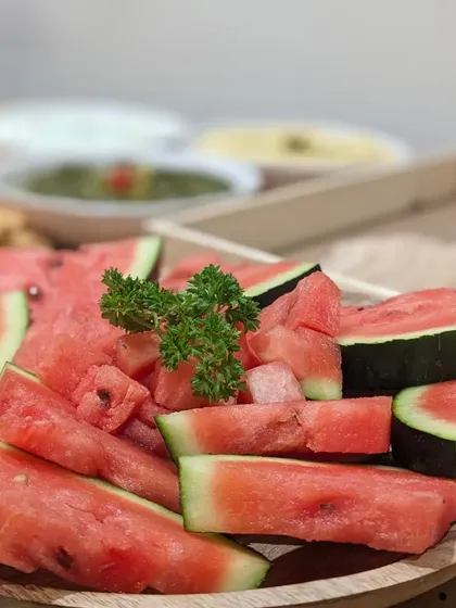 A simple and refreshing platter of freshly sliced watermelon, garnished with parsley. A healthy and hydrating option that complements a larger grazing spread.