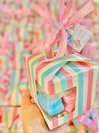 Holding one of the pastel striped baby shower favor boxes, which contains a candle and themed soaps.