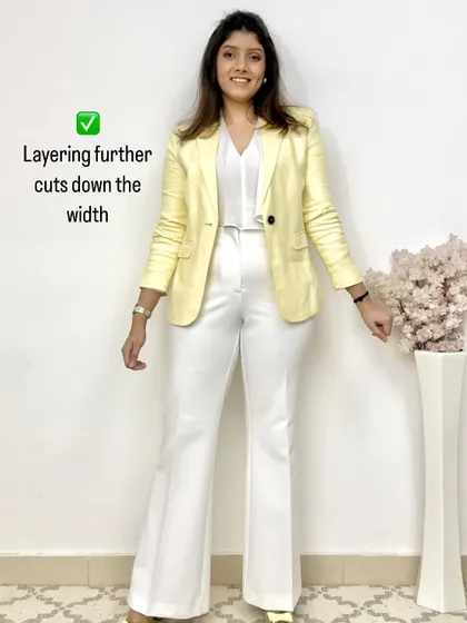 This image shows how adding a third layer, like this yellow blazer, over a monochrome white outfit further cuts down perceived width and creates a chic, polished look.