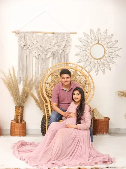 A full view of my boho-themed studio setup, featuring a wicker peacock chair, macrame hangings, and dried grasses. The couple's soft pink and blue outfits complement the natural tones.