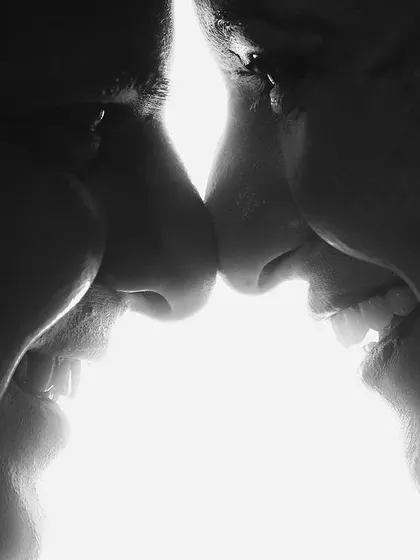 A dramatic black and white silhouette of a couple nose-to-nose. The bright backlighting creates a striking contrast, focusing entirely on their connection and joy.