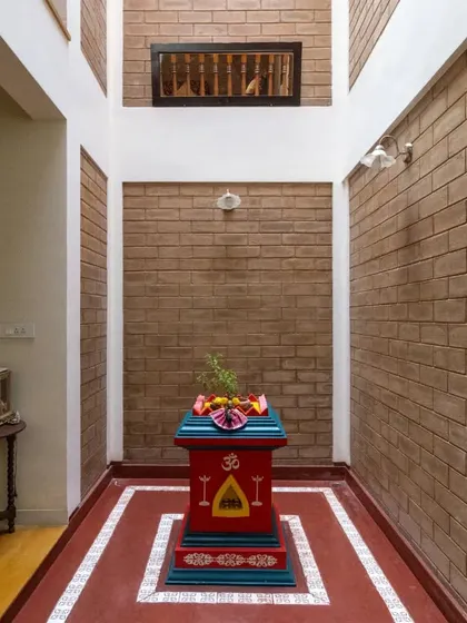 The central courtyard, a core feature of the home, housing a traditional Tulasi Katte against a backdrop of exposed brick, connecting the home to both nature and spirituality.