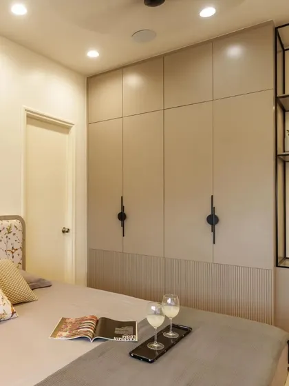 A full view of the beige bedroom, showing the custom bed, wardrobe, and integrated open shelving. The design is a perfect example of mixing minimalism with statement pieces.