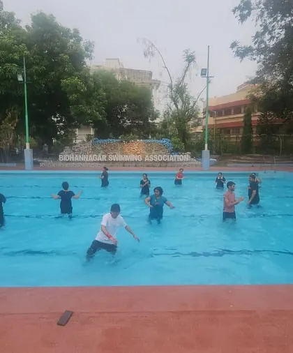 A wide angle of the class spread out in the pool during an aqua yoga session, focusing on balance and stretching.