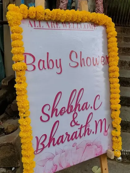 A personalized welcome board for a baby shower. The sign is framed with traditional yellow marigold flowers, setting a warm and welcoming tone for the event.