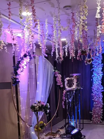 A dreamy and whimsical engagement or reception backdrop. This setup features a ceiling of hanging pink and white wisteria, a circular arch with fairy lights, and dramatic uplighting to create an enchanting atmosphere.