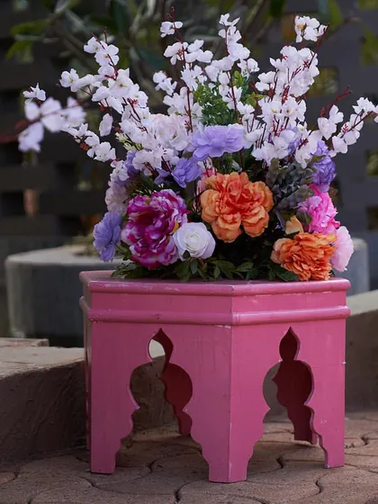 A beautiful floral arrangement in shades of pink, purple, and orange, placed on a decorative pink stool. These small touches of color brighten up any corner.