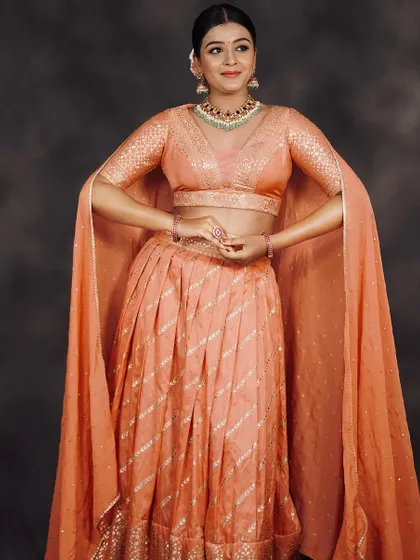 The cape sleeves of this peach lehenga add a touch of modern drama and are perfect for creating movement in photos.