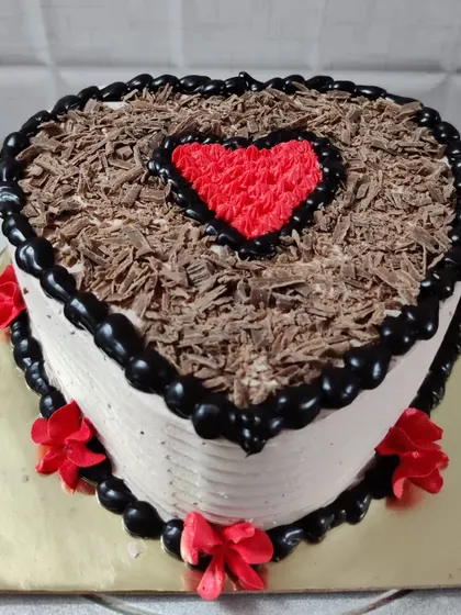 A heart-shaped black forest cake. The top is covered with chocolate shavings and a piped red heart in the center.