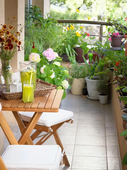 A traditional and charming flower-filled balcony. A simple wooden folding table and chairs provide a lovely spot for a quiet breakfast surrounded by blooming plants.