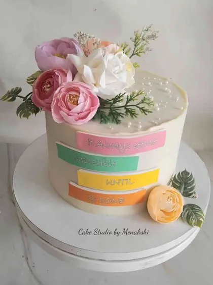 A cake with an inspiring message. This no-fondant design is decorated with fresh flowers and colourful banners that read, "It always seems impossible until it's done."