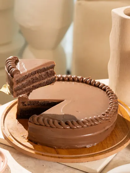 The perfect slice being lifted from a classic, glossy chocolate cake. This shot is all about the clean lines and the promise of a rich, moist dessert.