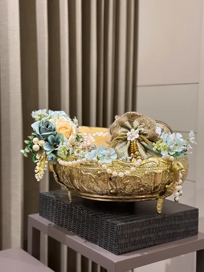 An elegant, footed metal bowl filled with beautifully wrapped gifts and decorated with soft blue and cream florals. This is a sophisticated choice for anyone who appreciates classic design.