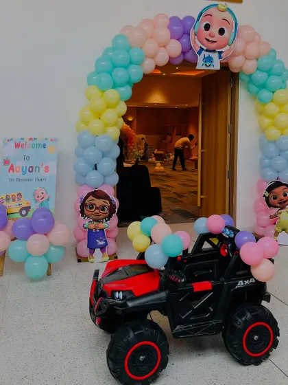 A Cocomelon-themed entrance with a pastel balloon arch, character cutouts, and a toy car for the birthday boy's grand entry.