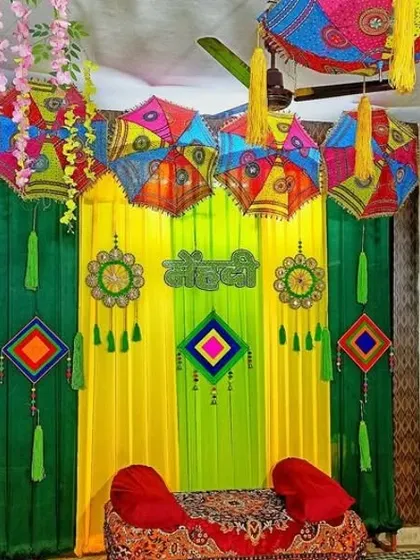 A Mehendi seating area with a backdrop of green and yellow drapes, decorated with hanging umbrellas and dreamcatchers.