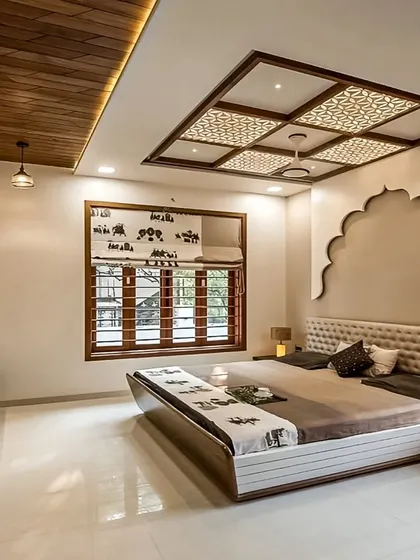 This bedroom blends modern and traditional Indian design elements, with a Jharokha-style arch on the accent wall and a beautiful jaali-patterned false ceiling.