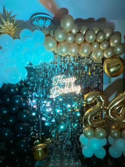 A cool and modern 24th birthday setup with a shimmer wall, neon sign, and balloon arrangement in black, gold, and aqua blue.