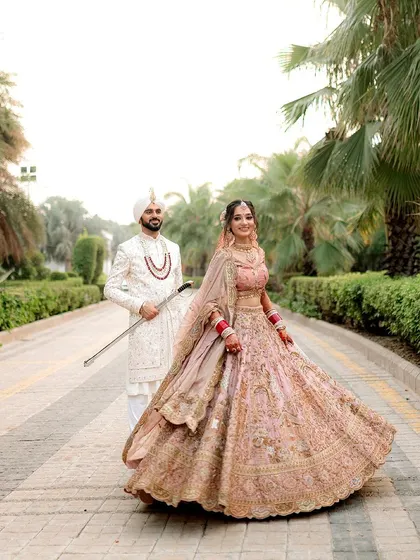 A stunning portrait of the Sikh bride twirling, her beautiful pastel lehenga in full motion, with her groom looking on.