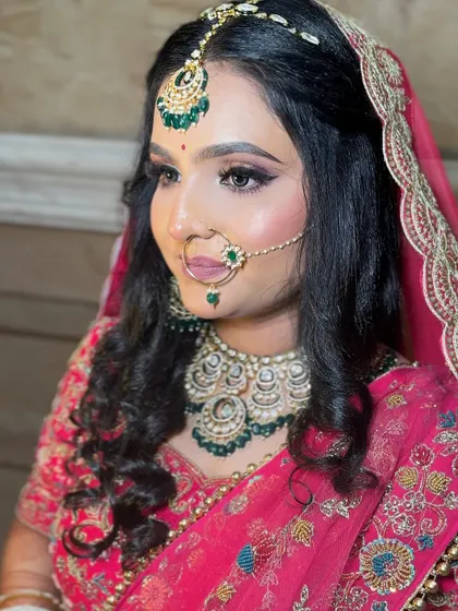 A side profile of a bride in a pink lehenga, showing off her beautiful hairstyle and the elegant draping of her dupatta.
