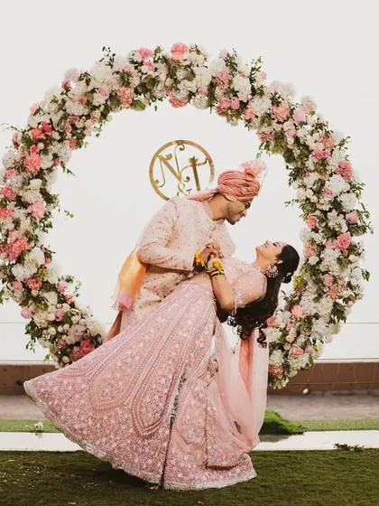 A fun and romantic dance pose in front of a circular floral arch. The bride's lehenga twirls beautifully, adding a sense of movement and joy to this stunning portrait.