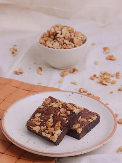 Our Walnut Brownies served on a plate, with a bowl of walnuts in the background to showcase the fresh, key ingredient.