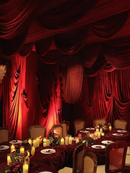 An immersive dining experience designed for an intimate engagement. The entire room is draped in red velvet, with tables set for a royal feast, illuminated by candlelight and grand chandeliers.