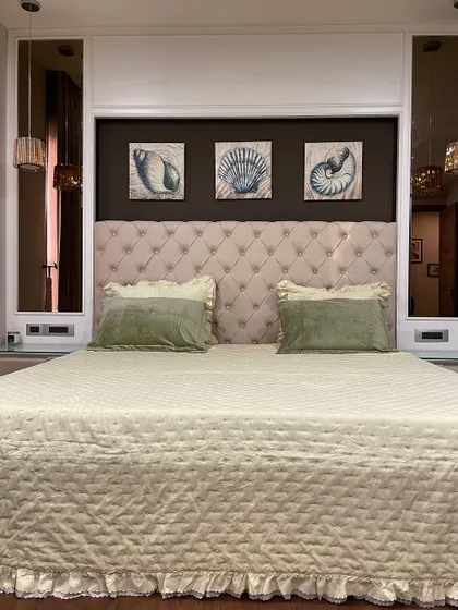 We designed this cozy master bedroom with a classic tufted headboard in a soft beige fabric. The wall behind the bed is flanked by tinted mirrors, which add depth and reflect the light from the pendant lamps.
