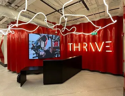 The reception area at a DLF Thrive gym, featuring a dramatic red corrugated wall and a custom 'noodle' light installation. The angular black desk and neon branding create a powerful first impression.