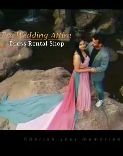 A couple posing on rocks by the water in a multi-colored trail gown. The blend of pink, blue, and green in the fabric mimics the natural colors of the landscape.