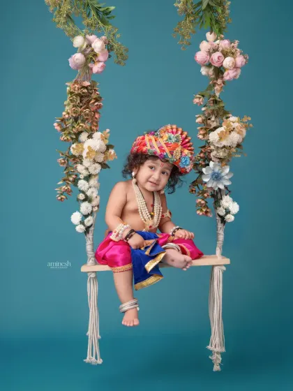 Another angle from the floral swing setup, showing your little one dressed as Krishna, holding a flute. The simplicity of the background makes the colorful outfit and flowers stand out.