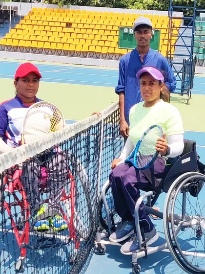 Two wheelchair tennis players and a coach by the net at the AITA Tennis Championship in Chennai. This photo highlights the supportive team environment during high-stakes competitions.