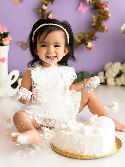 A happy moment from a butterfly-themed cake smash, showing a baby girl with a delightful, frosting-covered smile.