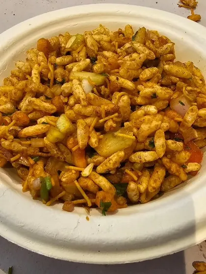 A close-up of our freshly made Bhel Puri. This light and crunchy snack is a mix of puffed rice, sev, onions, potatoes, and tangy chutneys, perfect for any time of day.