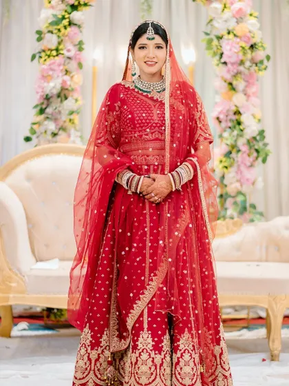 A full-length portrait of the bride in her stunning red wedding lehenga, showcasing her complete look from head to toe.