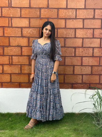A full view of the blue floral dress against a brick wall.