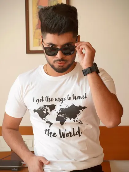 A confident portrait where the model adjusts his sunglasses. This action shot adds a dynamic and cool element to a simple t-shirt look.