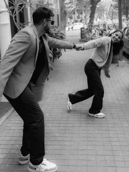 A playful black and white photo of a couple holding hands and pulling each other along a sidewalk. The motion and their smiles create a dynamic and fun-loving image.