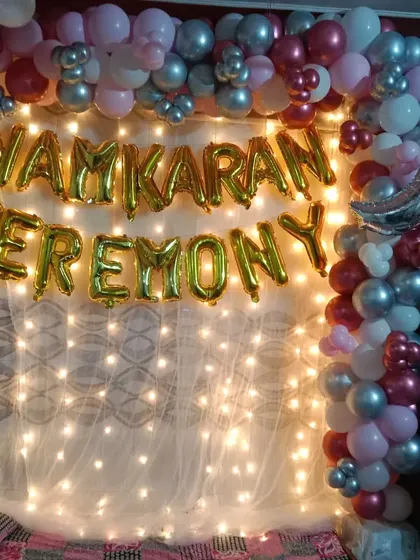 A special decoration for a Namkaran (naming ceremony). This setup features a wall of fairy lights, "Namkaran Ceremony" gold foil balloons, and a balloon arch in pink, silver, and maroon.