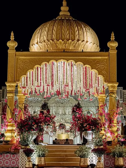 The main stage of our 'Shahi Jharokha' wedding, where a golden dome and intricate archways create a regal backdrop. The design, inspired by Udaipur's palaces, is adorned with cascading floral garlands for a touch of royal opulence.