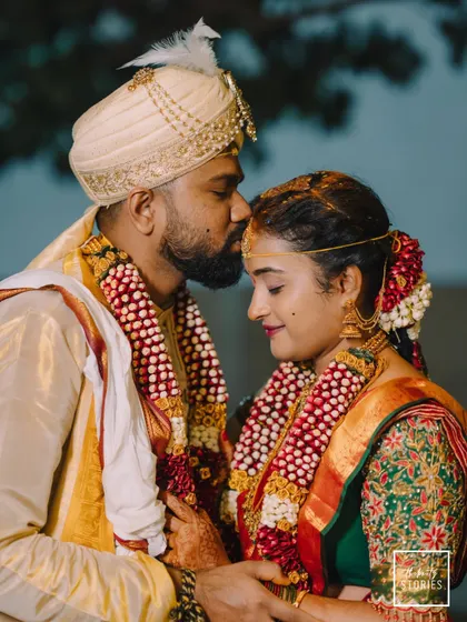 A tender moment between the newly married couple, with the groom placing a kiss on his bride's forehead. This close-up captures the emotion and the intricate details of their wedding attire and floral garlands.