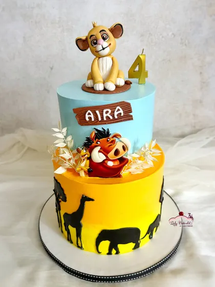 A two-tier Lion King cake for a 4th birthday. The bottom tier has a beautiful sunset safari silhouette, while the top features handcrafted Simba, Timon, and Pumbaa figures.