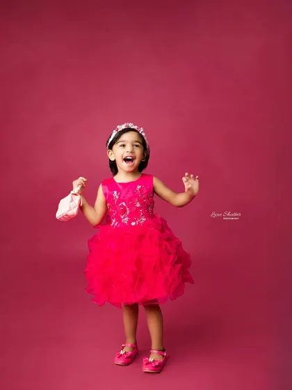 A vibrant and joyful portrait of a little girl in a bright pink dress, celebrating her birthday with a huge smile. This is perfect for capturing the energy of older toddlers.