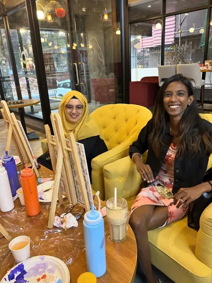 Two friends smiling and enjoying the relaxed, creative atmosphere of a sip and paint session.