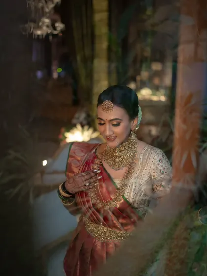 A candid moment of the bride, seen through the foliage. Her joyful smile and the intricate gold jewelry are the focus of this happy, natural portrait.